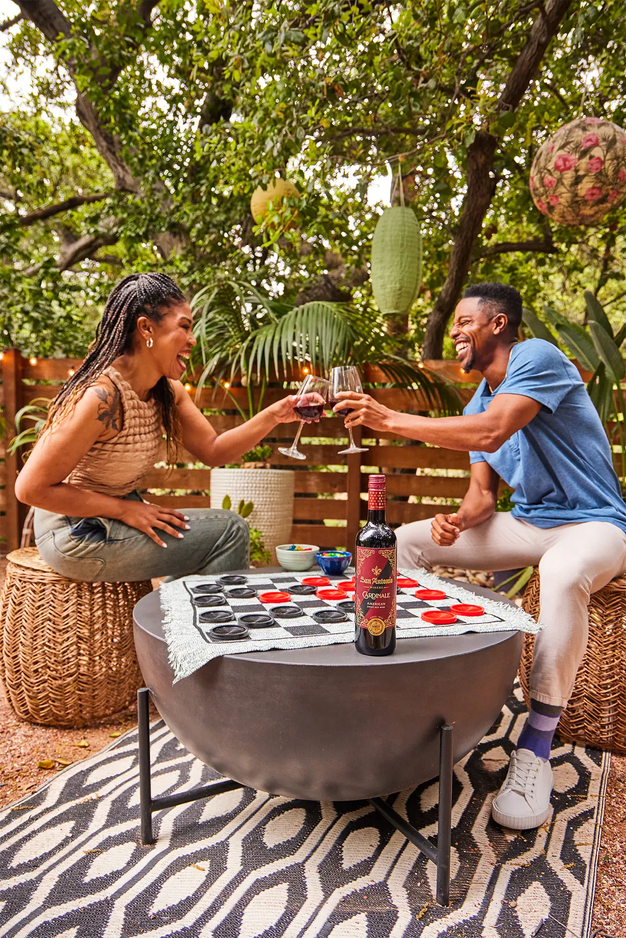 Two friends toasting with wine glasses over a game of checkers, with a bottle of San Antonio Winery Grignolino on the table.