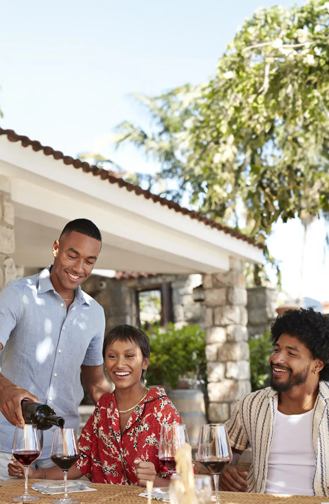 Three friends enjoying wine at an outdoor table, with one person pouring wine from a bottle of San Antonio Winery Port California sweet wine.